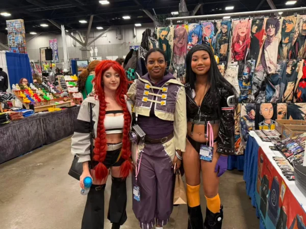Three convention attendees posing at the Komikku Villa anime merchandise booth